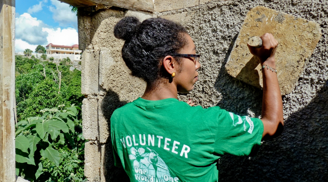A Projects Abroad volunteer plasters a wall during construction volunteering in Jamaica for a group. A group of volunteers works together to construct and plaster a house as part of building volunteer work in Jamaica.